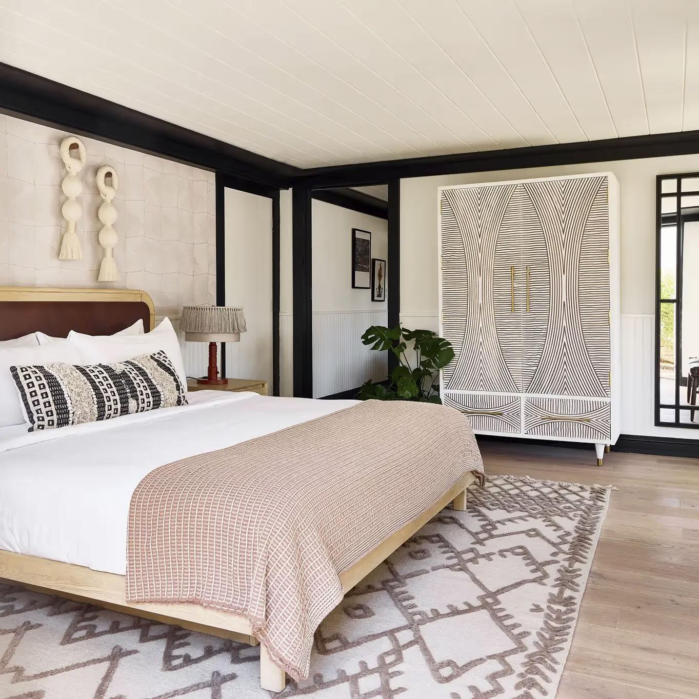 Modern bedroom with a bed, patterned rug, and decorative wall hangings.