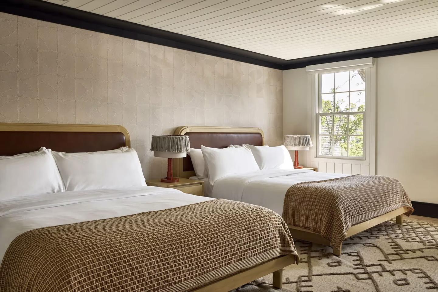 Two neatly made beds in a cozy, light-filled room with beige decor.