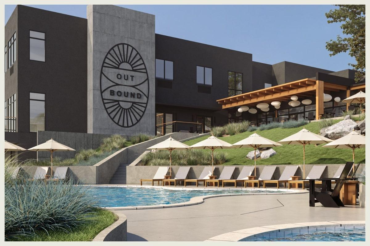 Modern hotel with a sign, pool, and sun loungers under umbrellas.