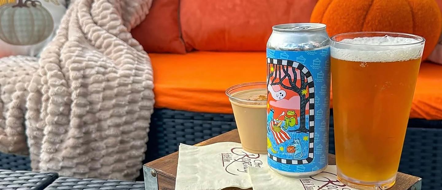 Colorful beer can, glass of beer, and coffee on a table with orange sofa and blanket.