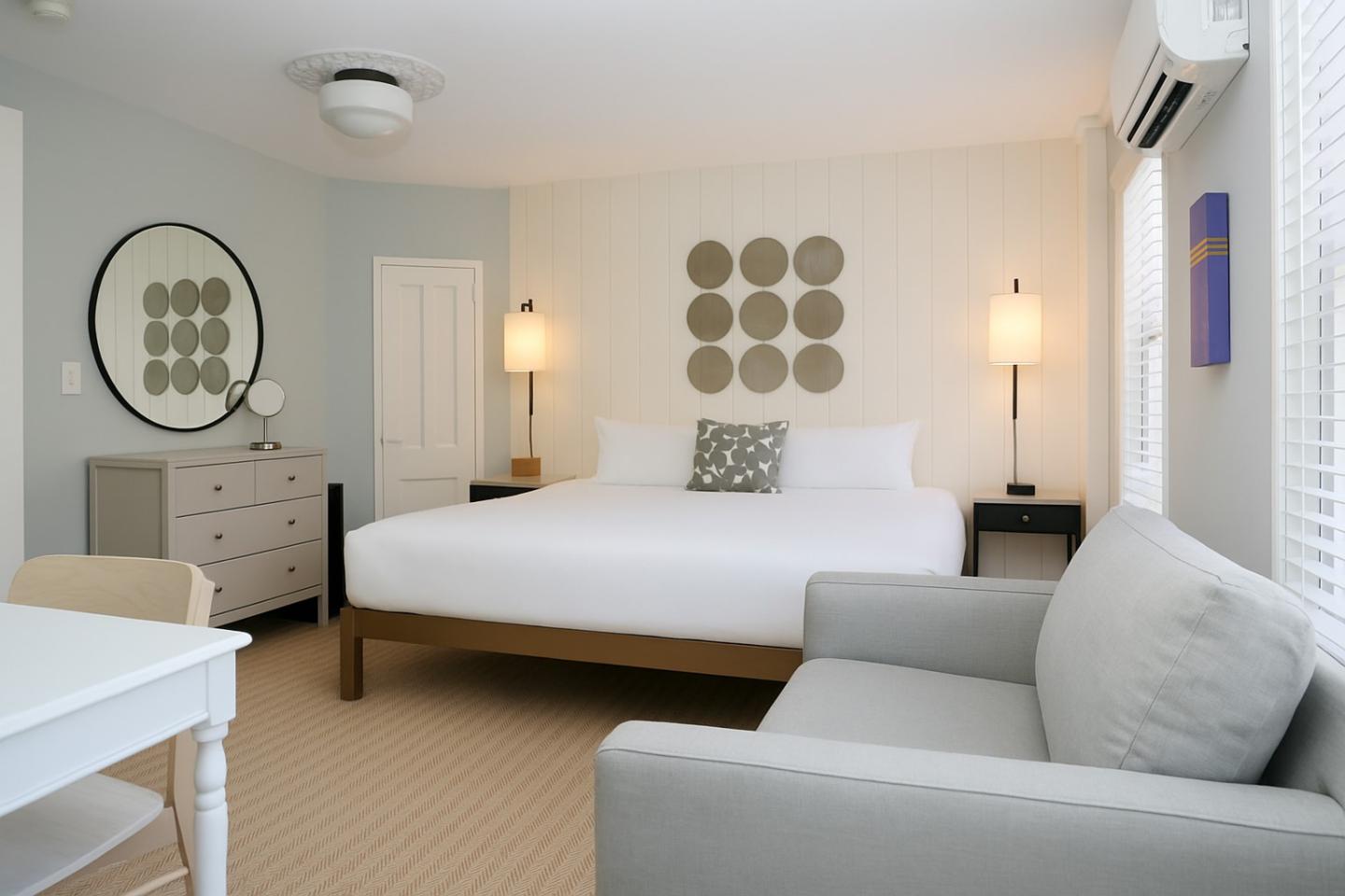 Modern hotel room with a king-sized bed, sofa, and decorative mirror.