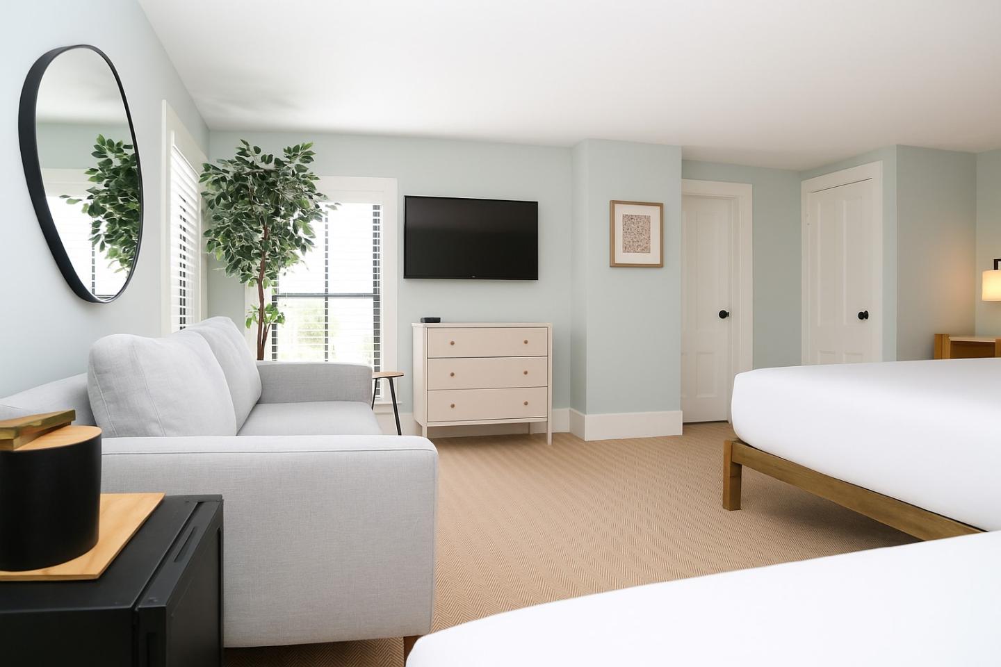 Modern hotel room with a sofa, wall-mounted TV, and two beds.