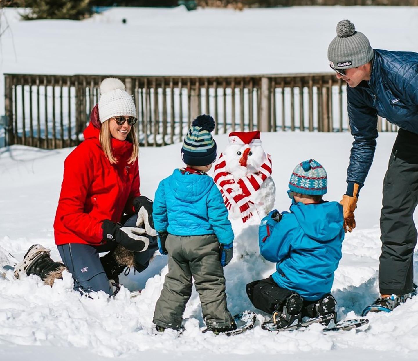 Family building a snowman in a snowy yard, wearing winter clothes.