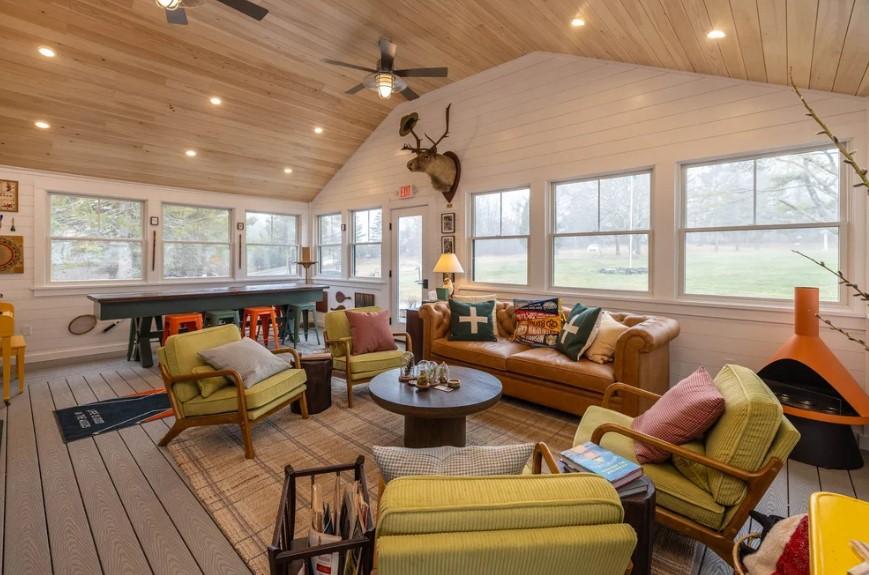 Cozy sunroom with sofas, armchairs, a ping pong table, and large windows.