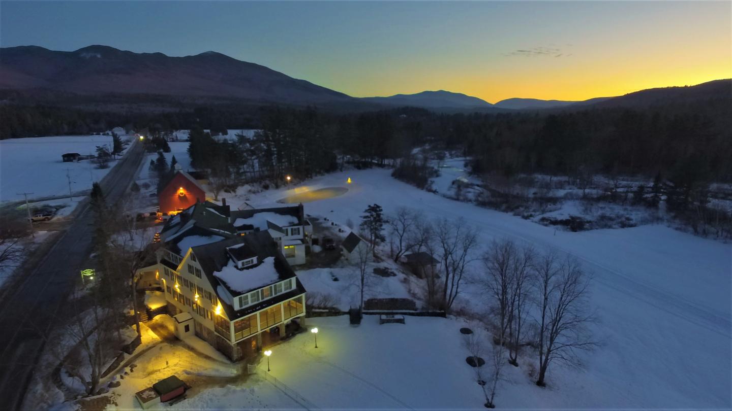Snowy village at dusk with warm house lights and mountain silhouette.