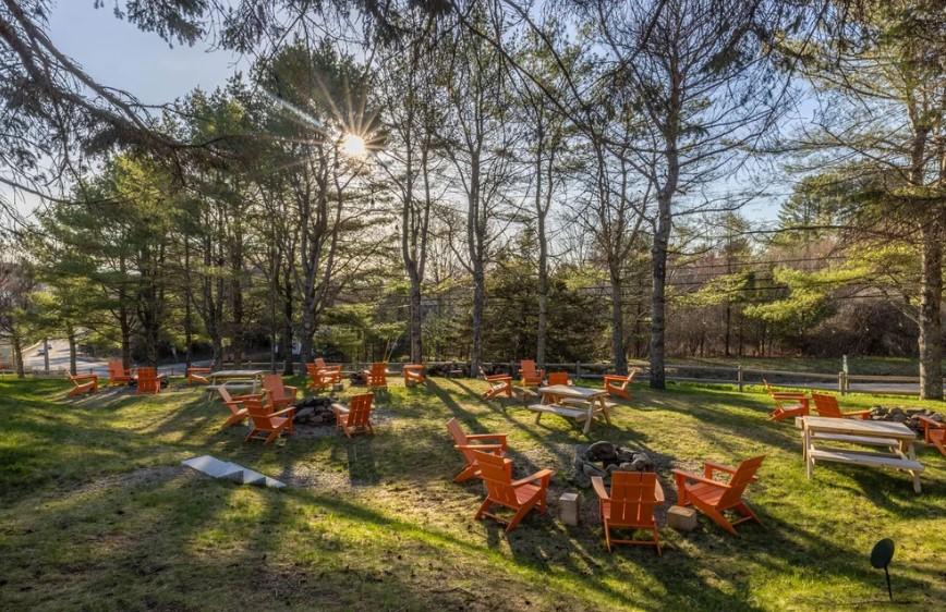 Sunny forest clearing with orange chairs and tables scattered on grass.