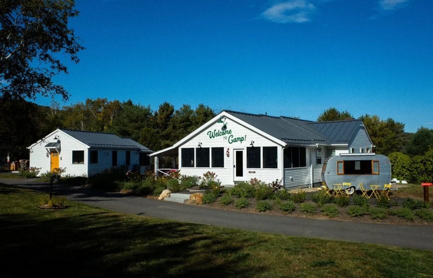 White building and trailer under blue sky, surrounded by trees and greenery.