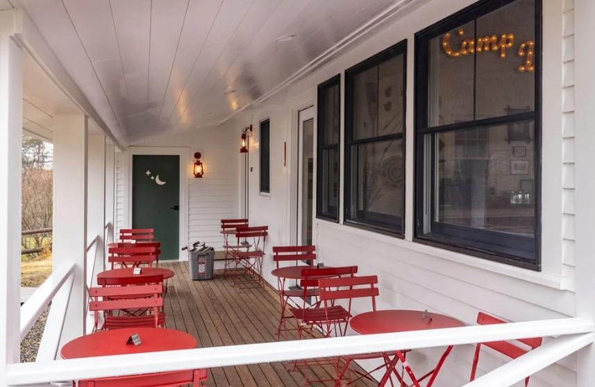 Red chairs and tables on a white porch with dark windows.