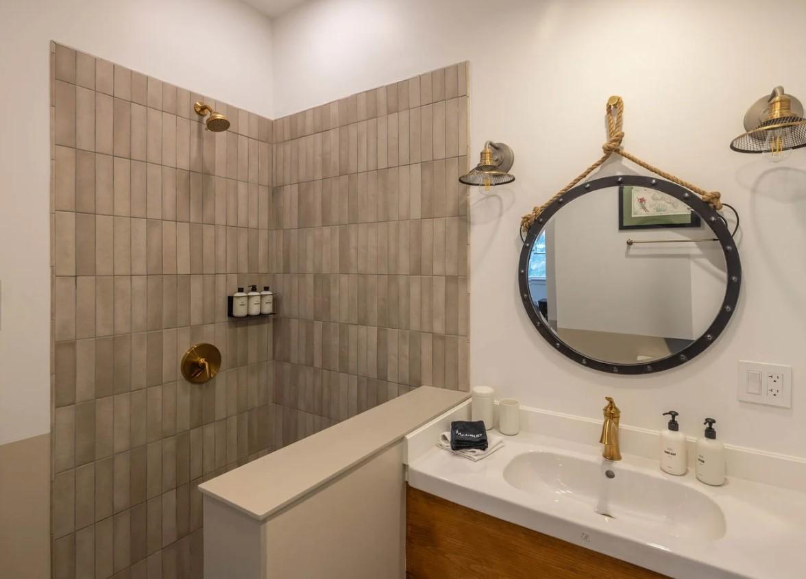 Modern bathroom with a round mirror, tiled shower, and brass fixtures.
