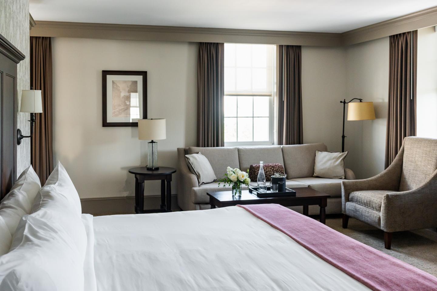 Guest room with a bed, seating area, and large windows.