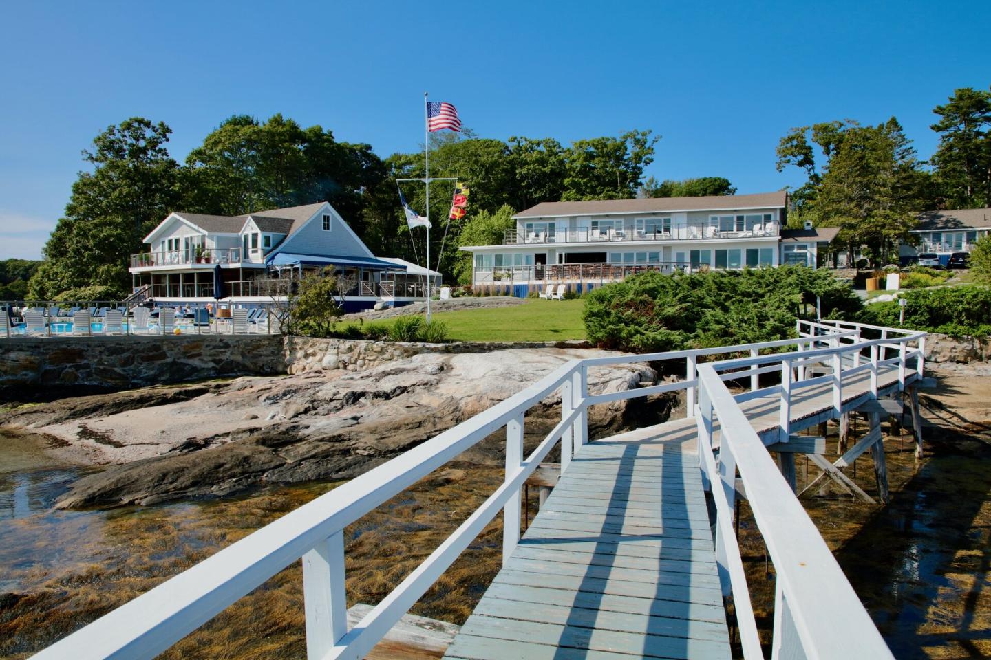 White dock leading to coastal houses with trees and blue sky.
