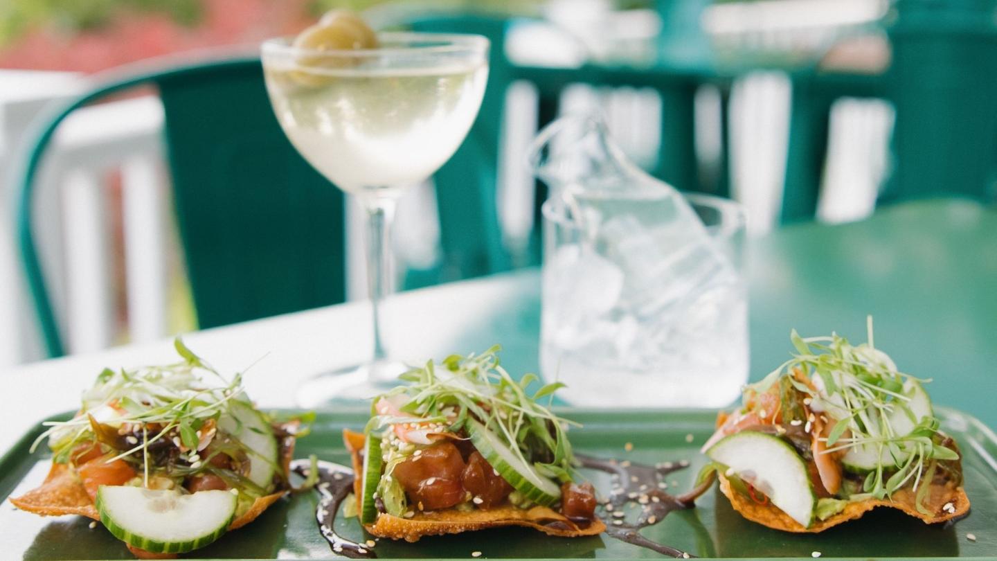 Tuna tartare on crackers with greens, wine glass, and water on a green table.
