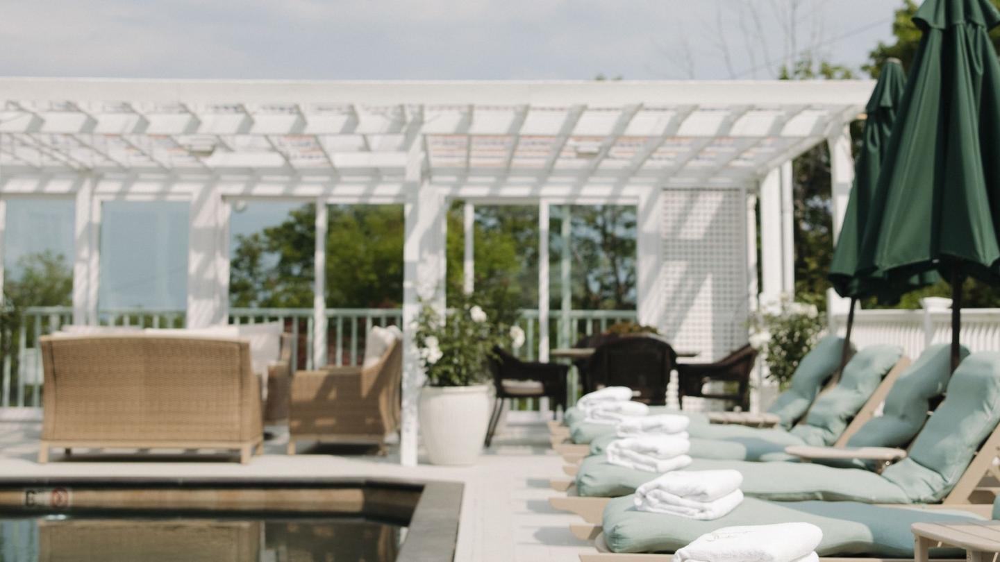 Poolside lounge chairs with folded towels under a pergola.