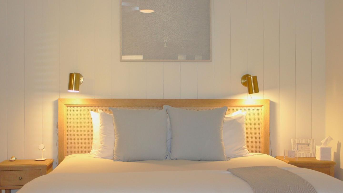 Cozy bed with soft lighting, neutral tones, and wall art above.