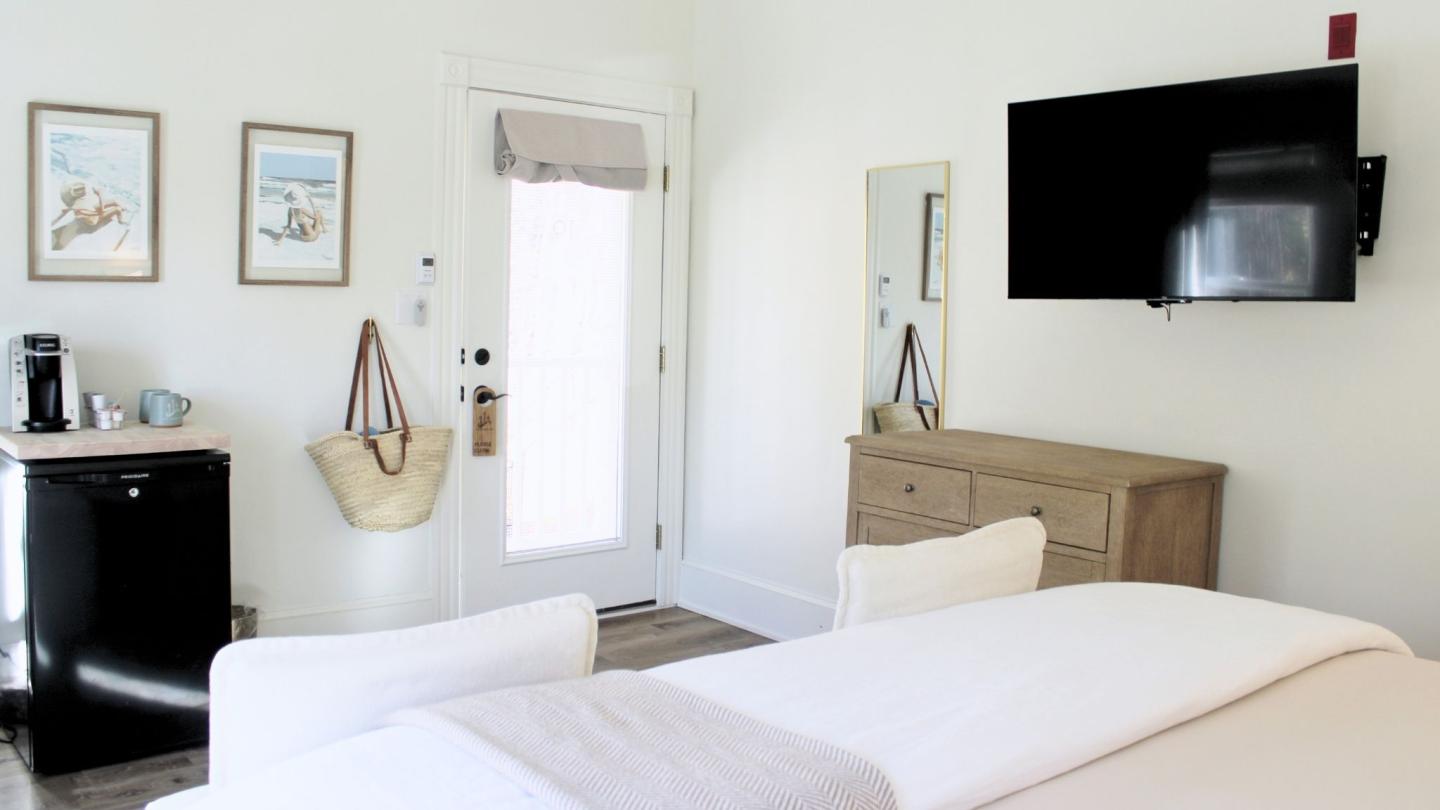 Cozy, white bedroom with bed, TV, dresser, and mini fridge.