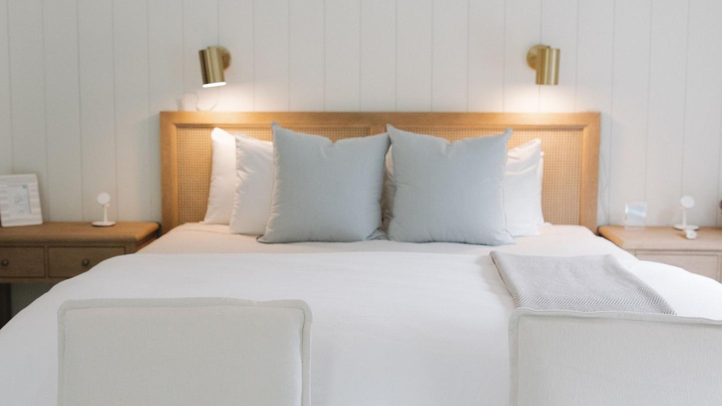 Bedroom with a neatly made bed, soft pillows, and wall-mounted lights.