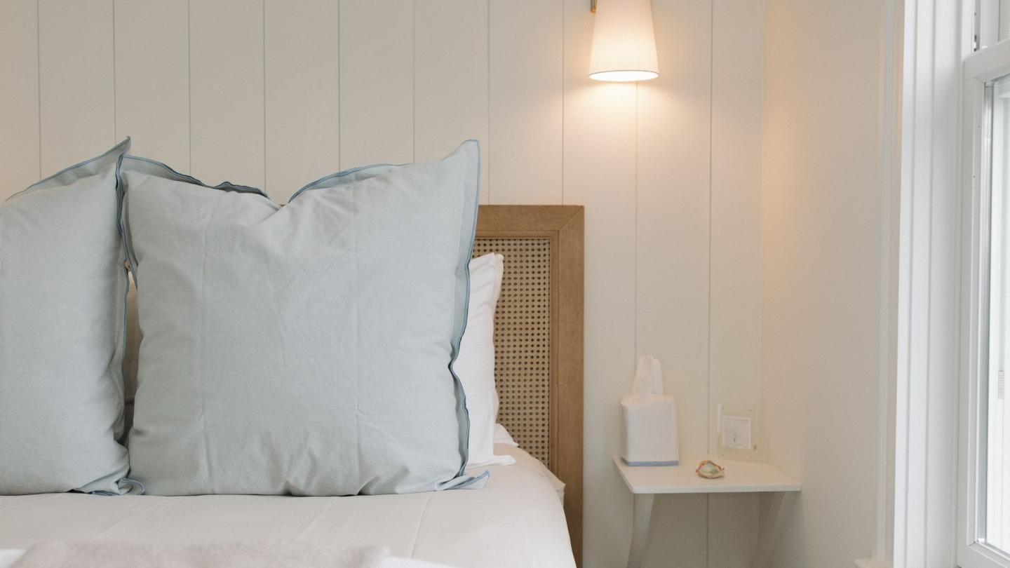 Bedroom with large pillows, wall lamp, and a small shelf with tissues.