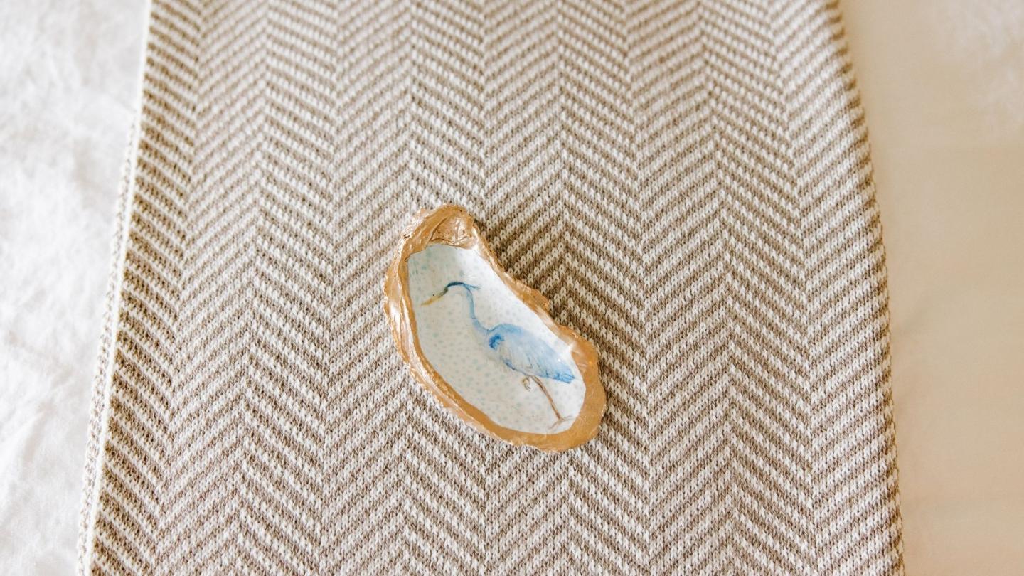 Wooden coaster with painted heron on textured gray fabric.