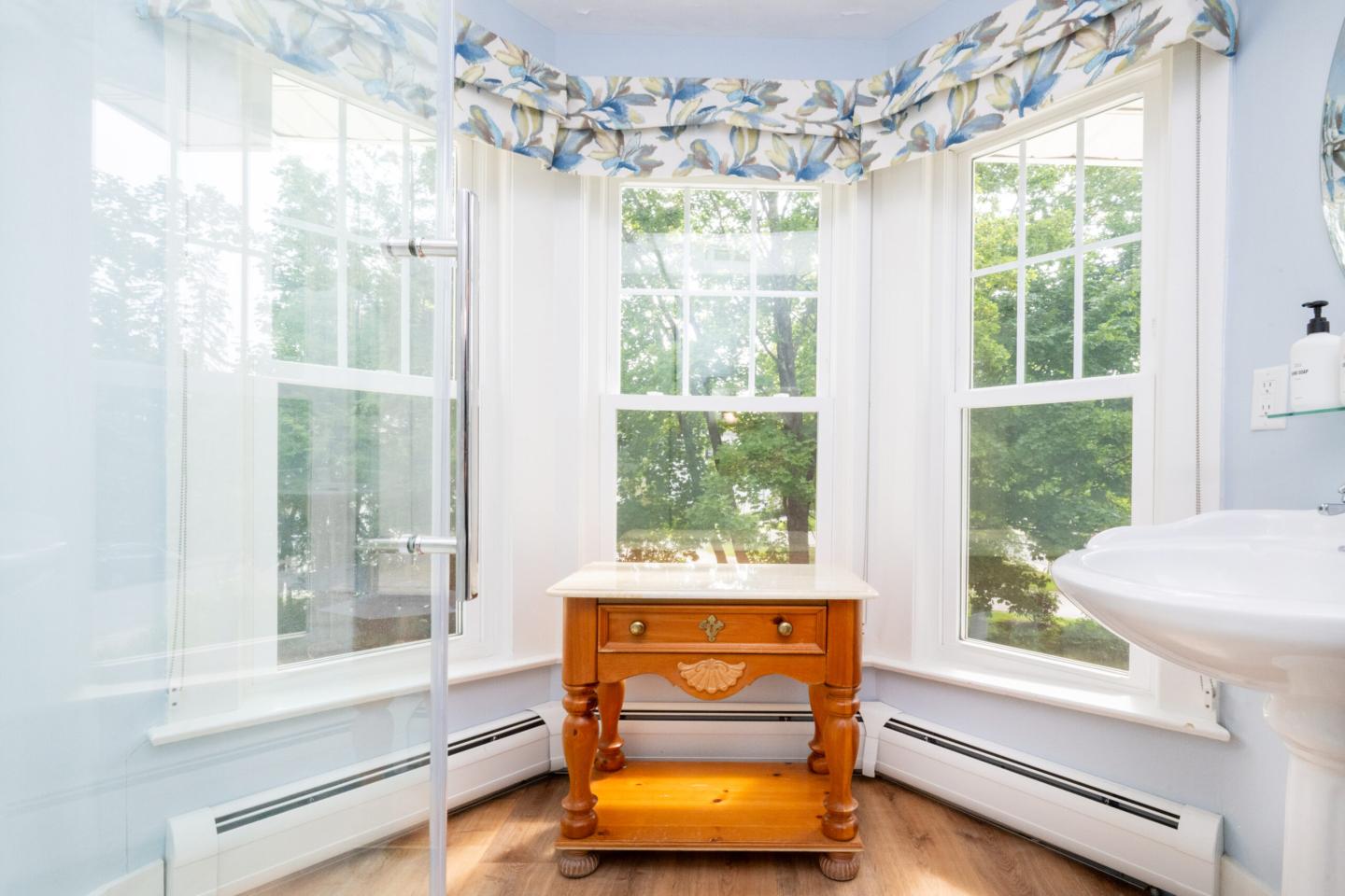 Bright bathroom with a wooden table by a large window, overlooking trees.