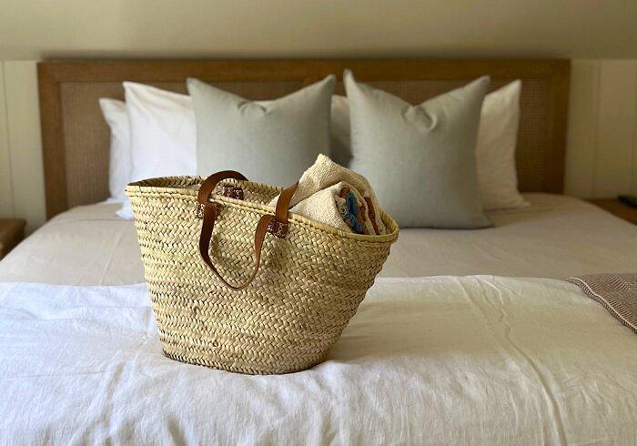 Woven basket on a neatly made bed with white pillows.
