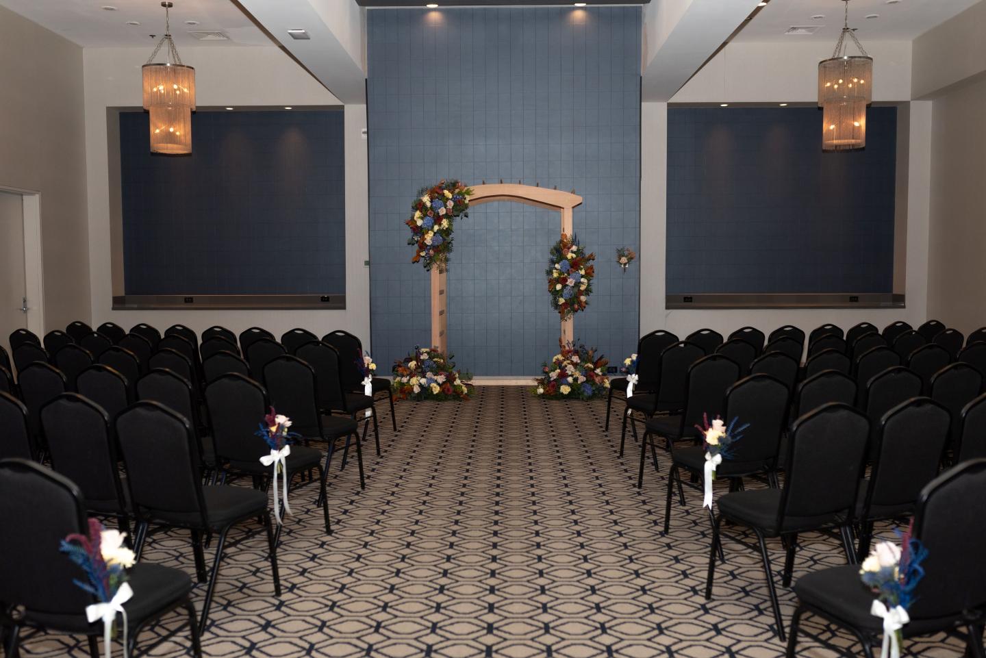Wedding ceremony setup with floral arch and rows of chairs in an elegant room.