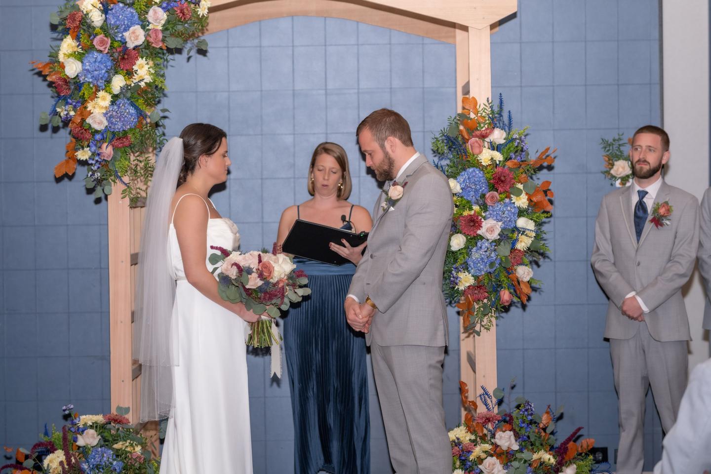 Wedding ceremony with couple under floral arch, officiant reading.