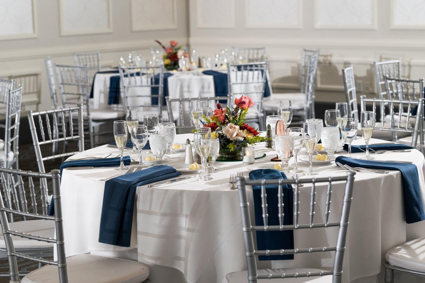 Elegant dining setup with round tables, navy accents, and floral centerpieces.