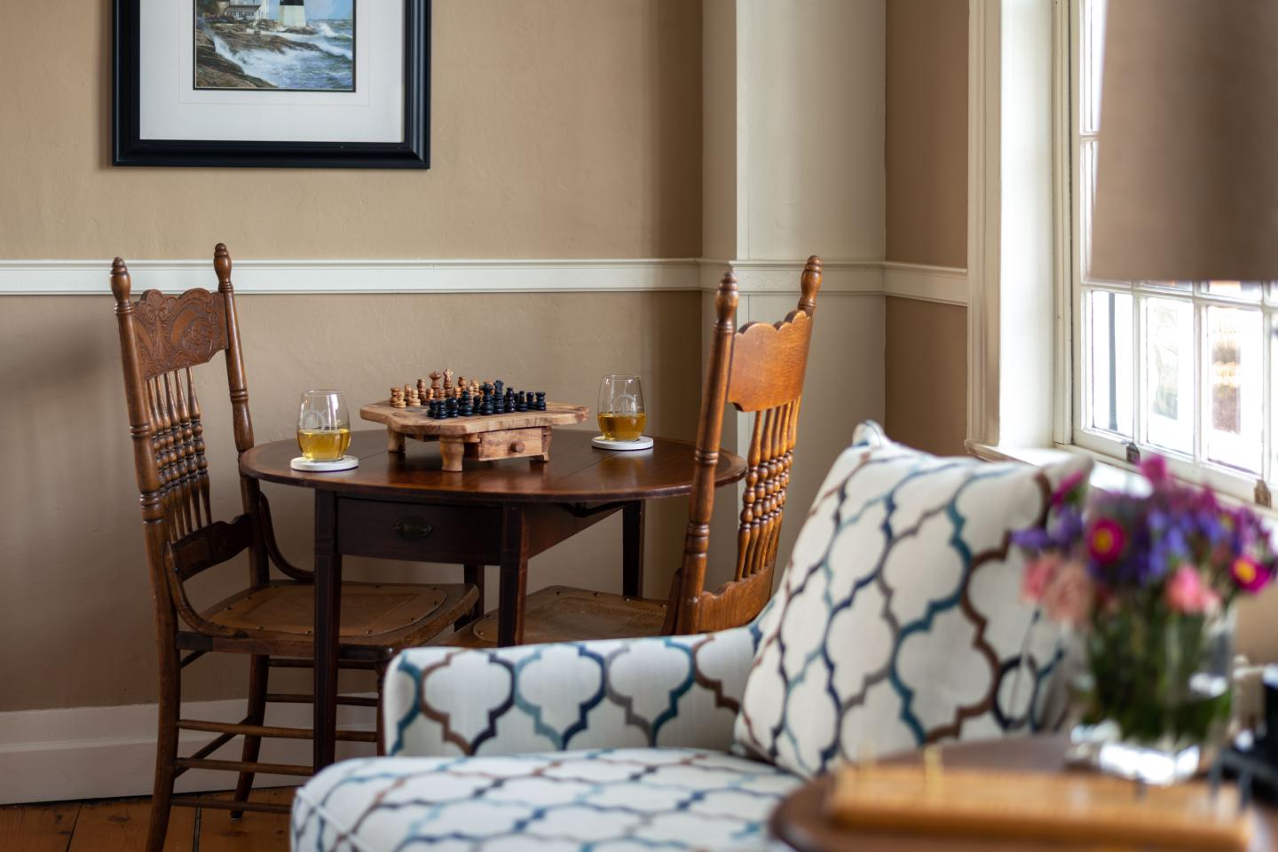 Cozy room with chessboard on table, wooden chairs, and floral couch.