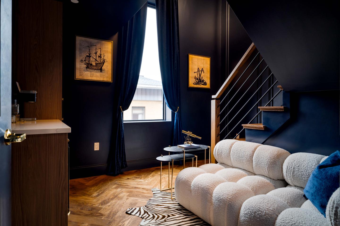 Cozy room with dark walls, a plush sofa, and a stairway with art on walls.