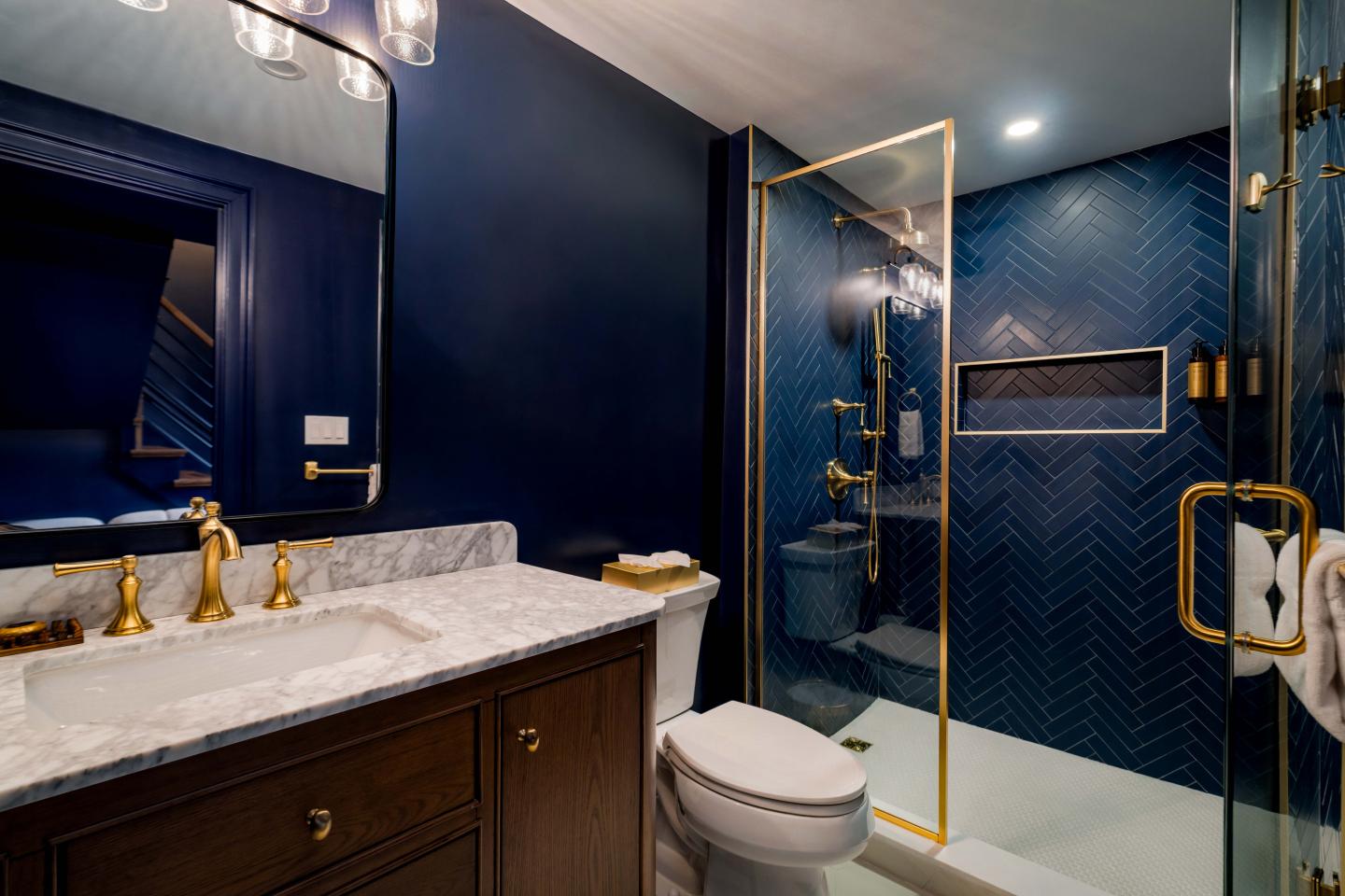 Modern bathroom with navy walls, gold fixtures, and a glass shower.