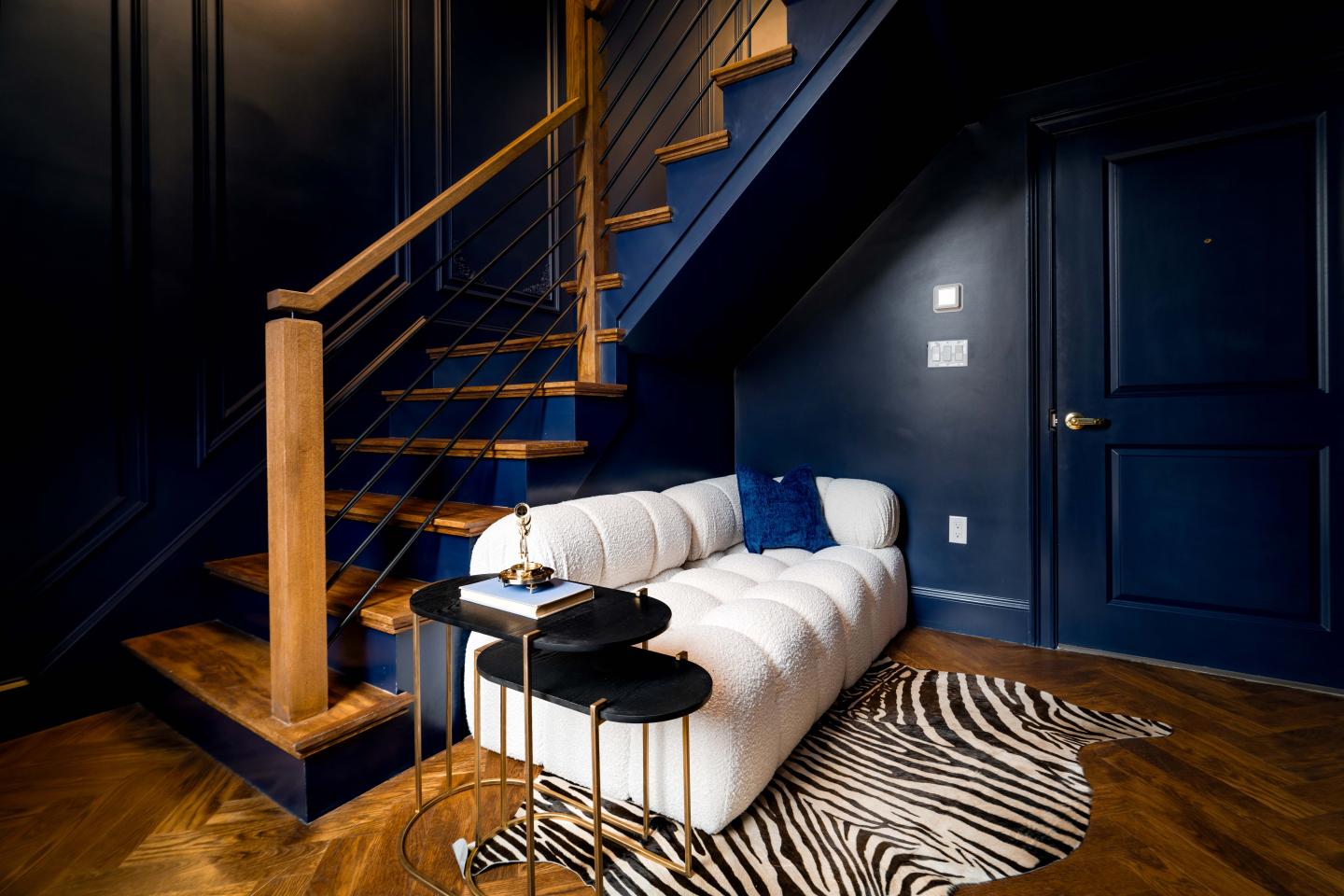 White couch under wooden stairs, zebra rug on dark hardwood floor.