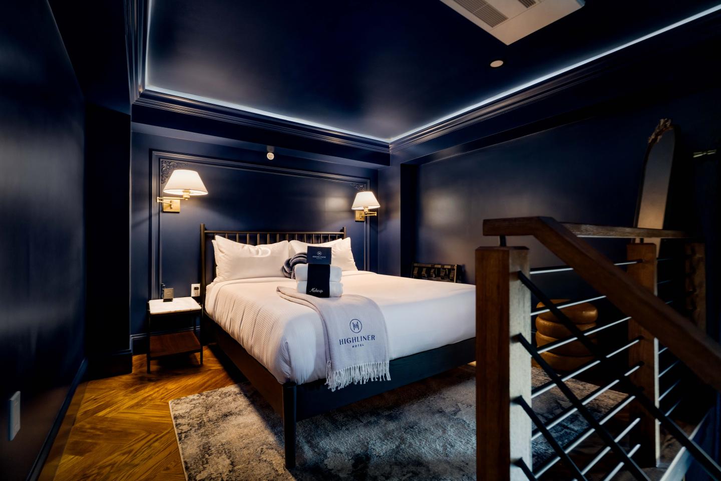 Stylish dark blue bedroom with a cozy bed, nightstand, and staircase.