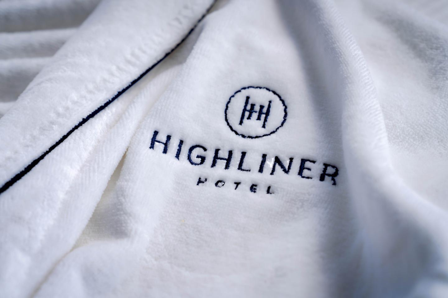 White fabric with "Highliner Hotel" logo embroidered in blue.
