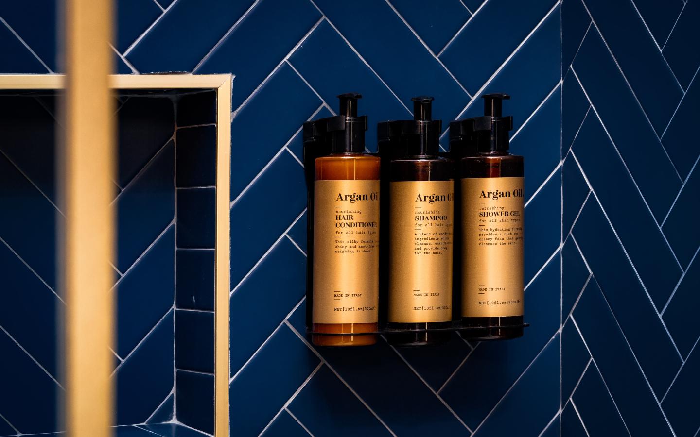 Three amber pump bottles against dark blue herringbone tiles.