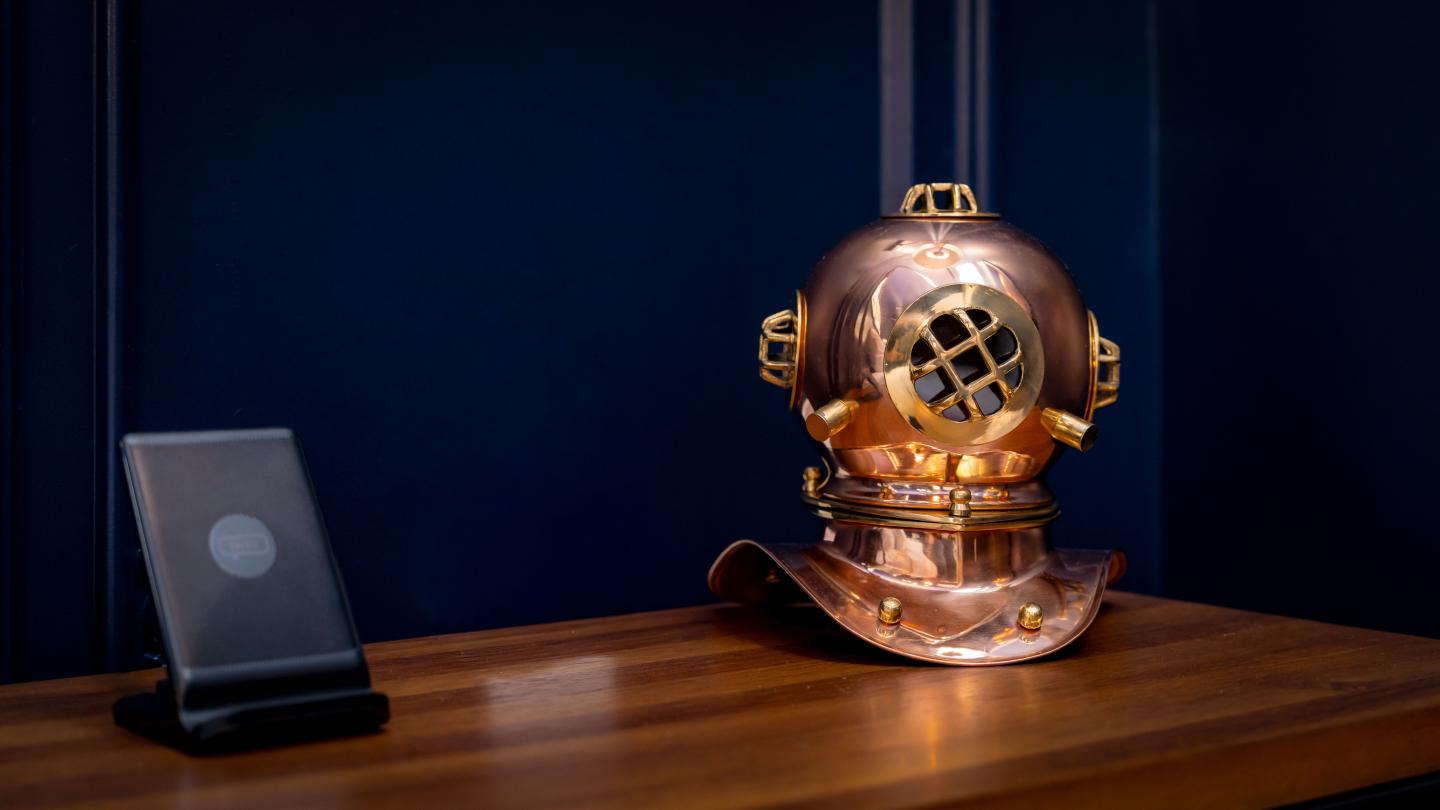 Antique diving helmet on wooden table with a black plaque.