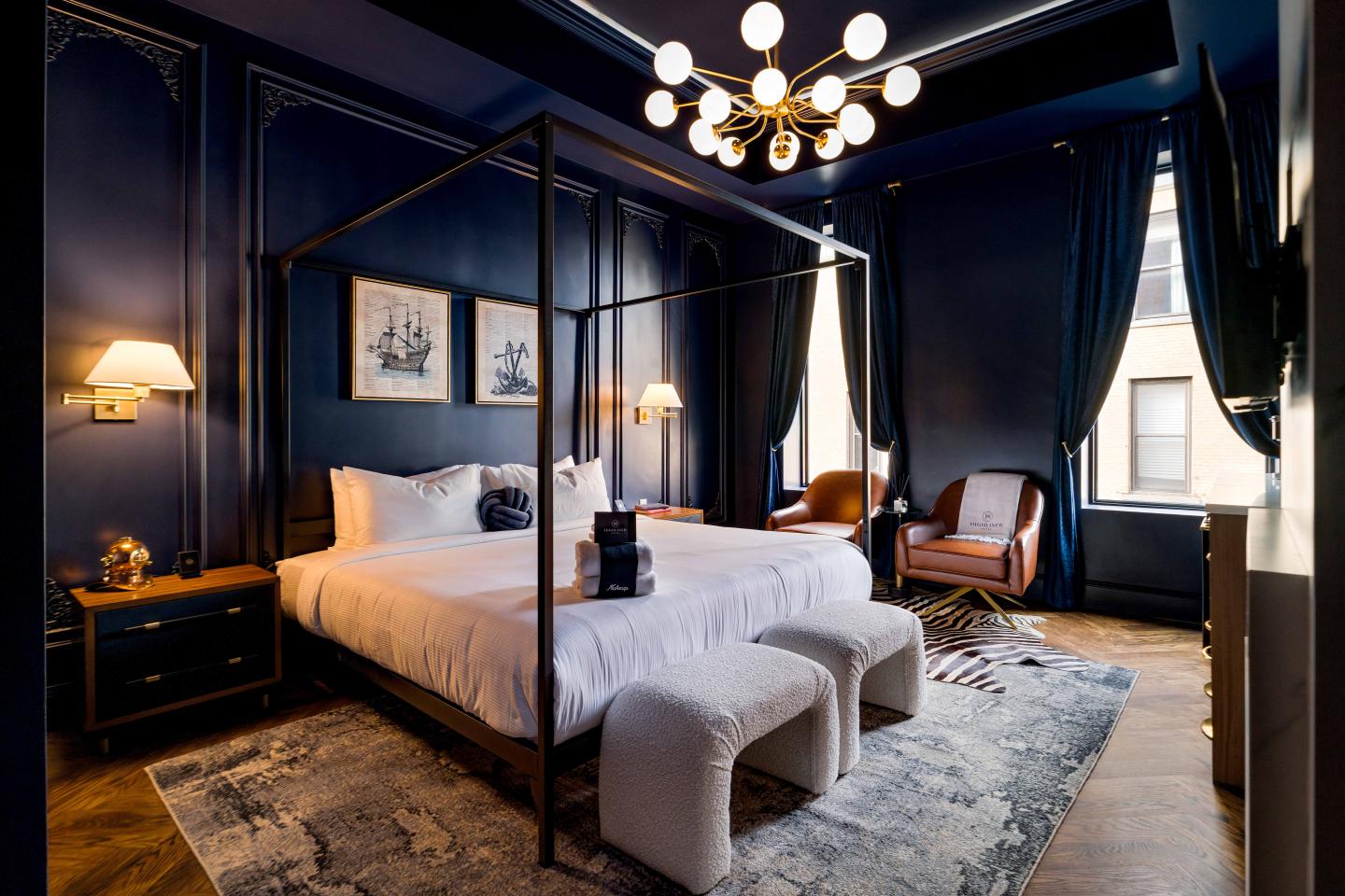 Elegant bedroom with dark walls, a canopy bed, modern lighting, and cozy seating.