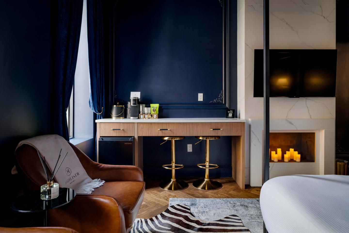 Cozy hotel room with brown leather chair, desk, and faux fireplace.