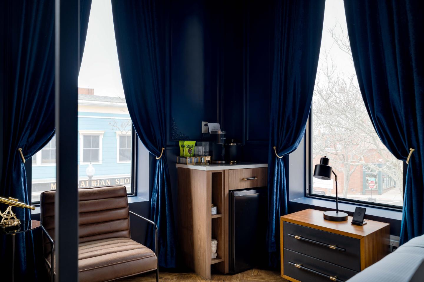 Cozy room with blue curtains, a chair, and a small kitchenette by the window.