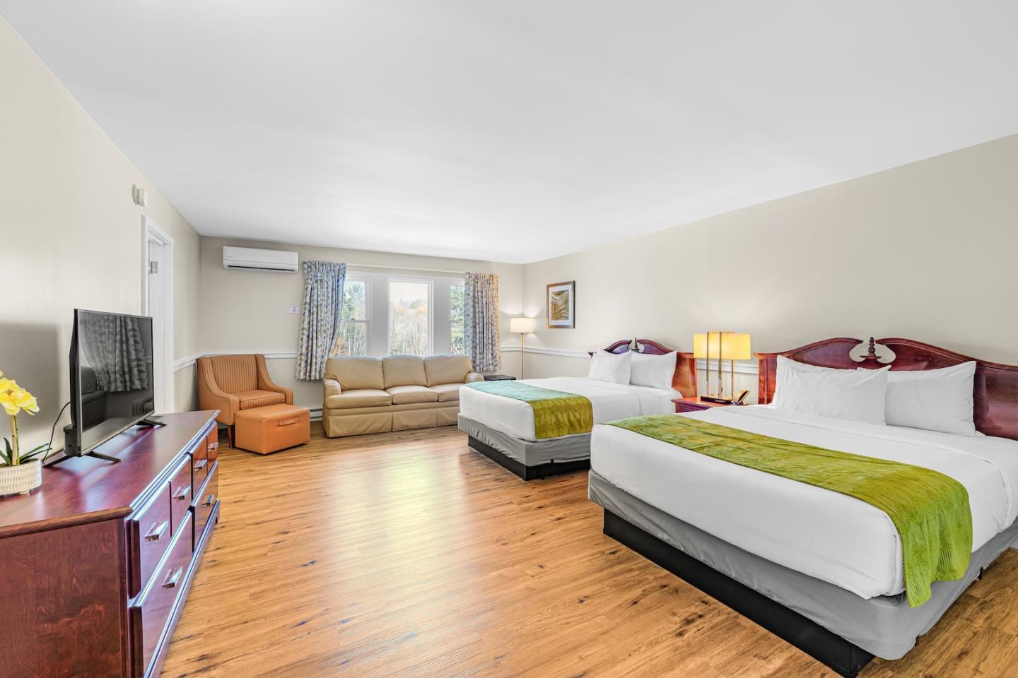 Spacious hotel room with two beds, TV, and seating area.