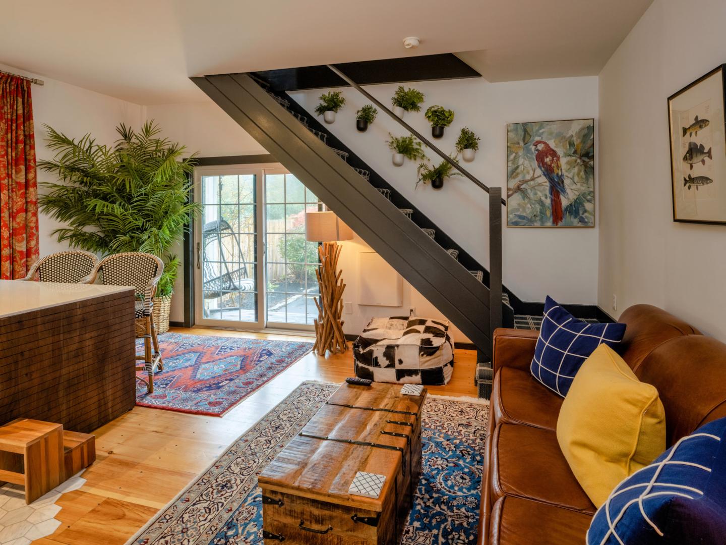 Cozy living room with plants, a cowhide rug, and a brown leather sofa under a staircase.