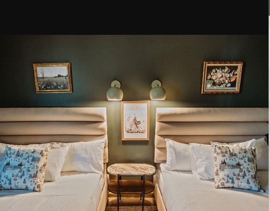 Two beds with patterned pillows, flanked by lamps and framed artwork on a dark wall.