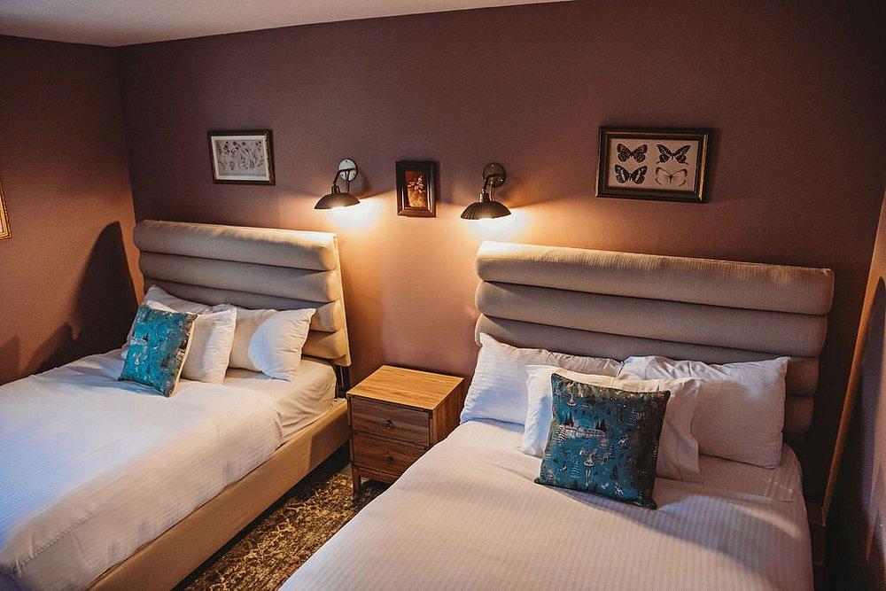 Two neatly made beds with teal pillows in a warmly lit hotel room.