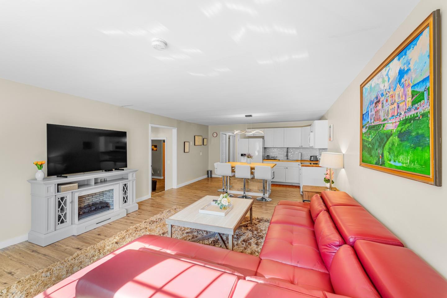 Spacious living room with red sofa, large TV, kitchen area, and colorful wall painting.