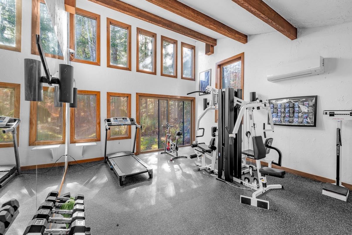 Bright home gym with treadmill, weights, and equipment, sunlight streaming through windows.
