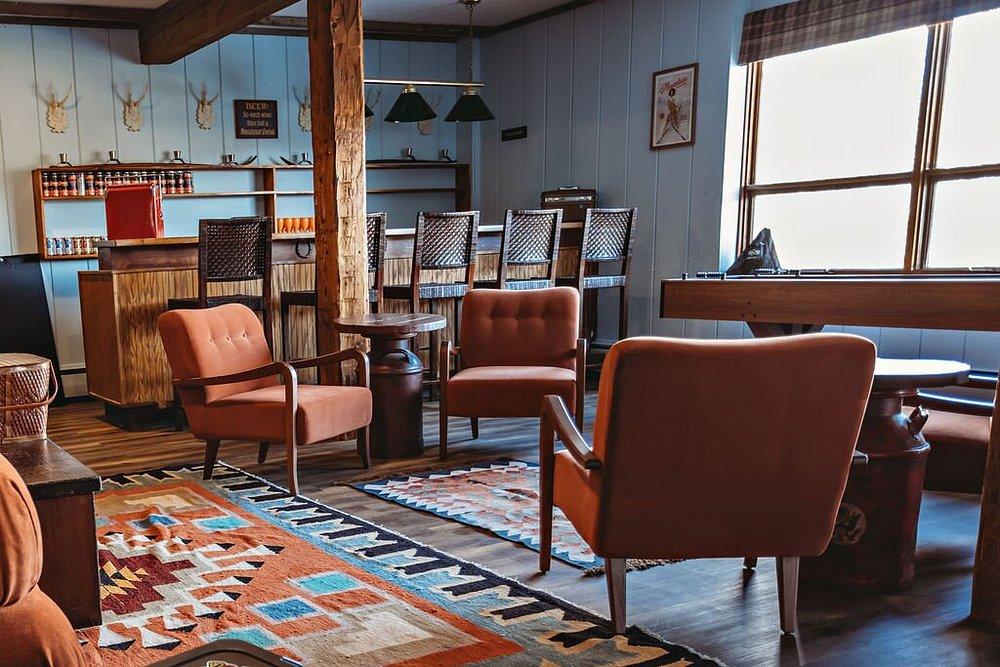 Cozy vintage lounge with brown chairs, patterned rug, wooden bar, and large window.