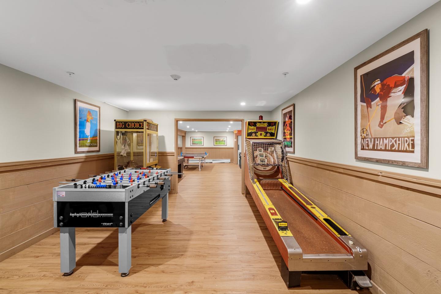 Game room with foosball, arcade machines, skee-ball, and framed posters on beige walls.