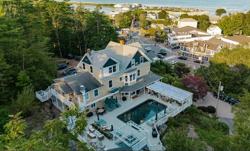 Aerial view of a large house with a pool, surrounded by trees and a coastal town.