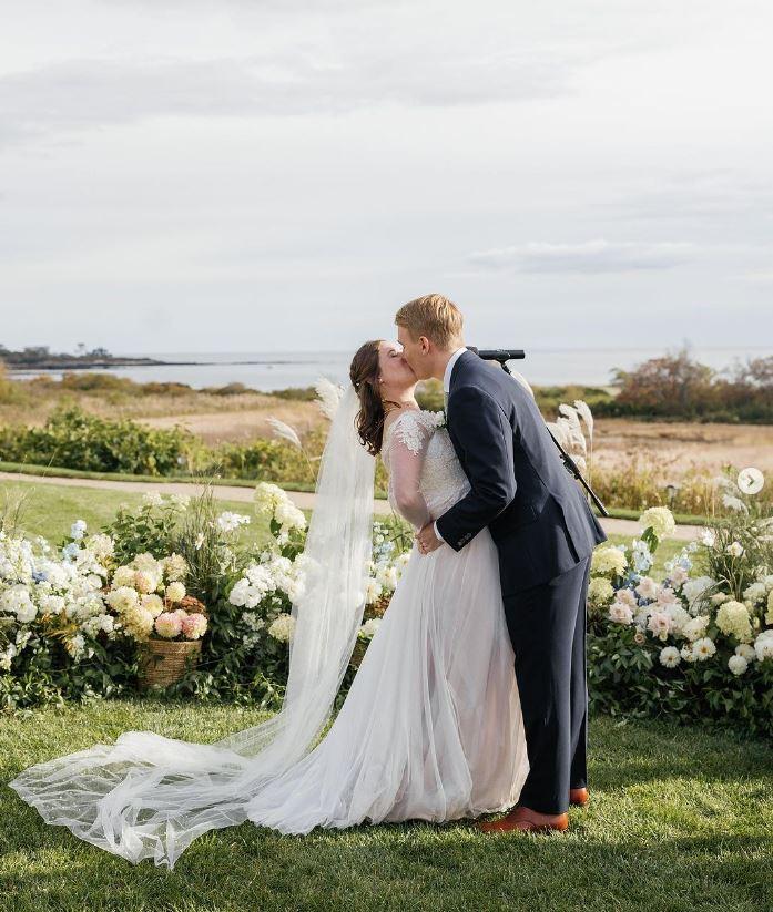 Bride and groom kissing outdoors, surrounded by flowers.