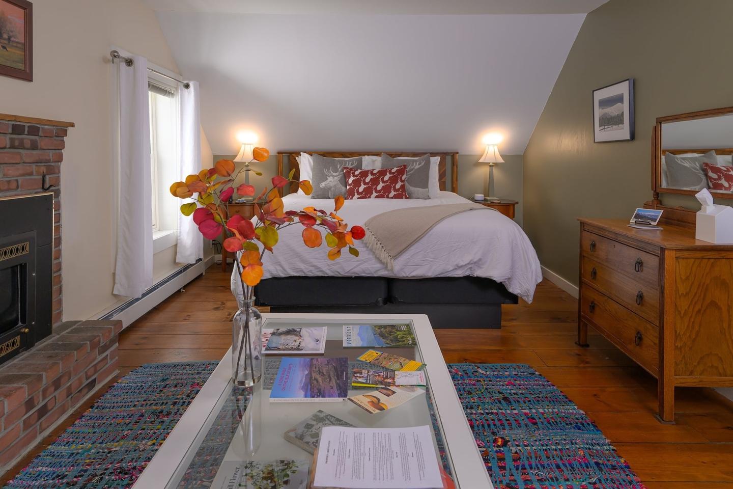 Cozy bedroom with a large bed, colorful rug, and a vase with flowers on a coffee table.