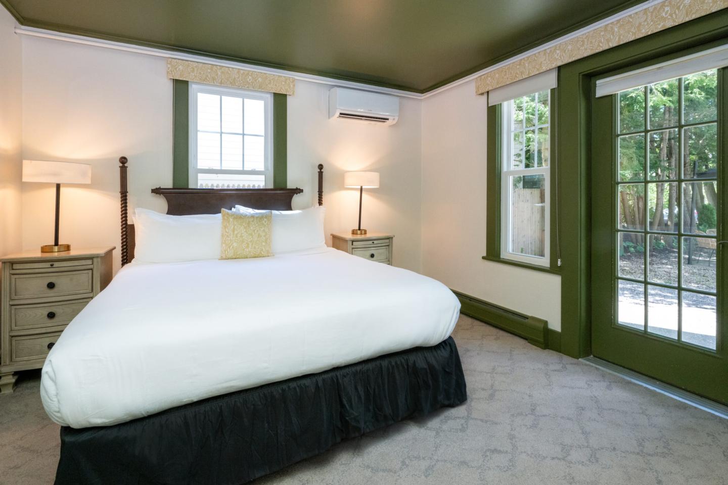 Bright bedroom with a large bed, two lamps, and a glass door leading outside.